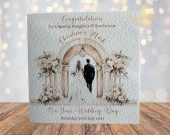 Puede incluir: Una tarjeta de boda con una ilustración de acuarela de una pareja caminando bajo un arco decorado con flores. La tarjeta dice "Felicidades a una hija y un hijo especiales Christina & Mark Por su día de boda Sábado 20 de julio de 2024".