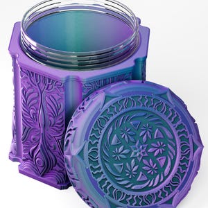 Pode incluir: Um recipiente de armazenamento cilíndrico com tampa de rosca, apresentando um acabamento degradê vibrante em roxo e azul-petróleo. O exterior e a tampa são decorados com padrões botânicos intrincados em relevo, incluindo motivos de folhas e flores.