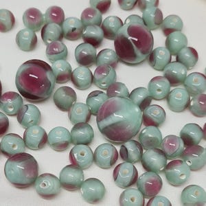 May include: A collection of green and pink swirl glass beads. The beads are round and have a smooth, glossy finish.