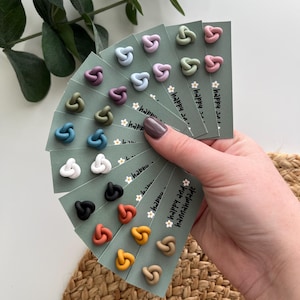 May include: Assortment of handmade polymer clay earrings in various colors, including green, blue, purple, pink, brown, orange, yellow, and white. The earrings are displayed on small cards with the text "happy and hannahmade".