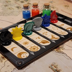 May include: A board game with a black game board featuring slots for tokens and the text "INERT WANING STRONG." The game includes various tokens representing elements like sun, moon, leaf, and fire, along with small glass bottles filled with colored liquids.