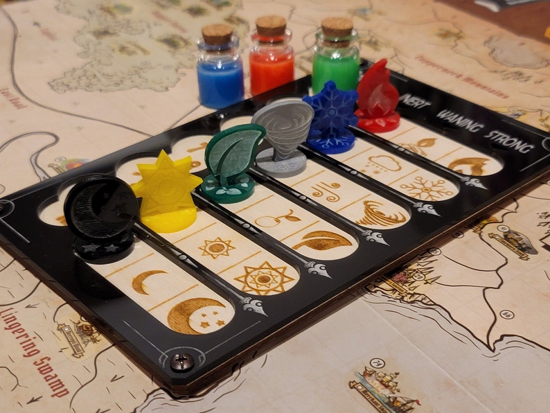 May include: A board game with a black game board featuring slots for tokens and the text "INERT WANING STRONG." The game includes various tokens representing elements like sun, moon, leaf, and fire, along with small glass bottles filled with colored liquids.