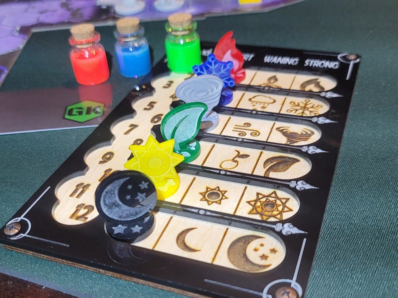 May include: A wooden game board with a black frame, featuring etched designs and numbered slots. Colorful game pieces include potion bottles and elemental symbols. The text "Waning Strong" is visible.