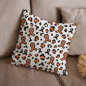 May include: A white cushion with a pattern of orange awareness ribbons and black leopard spots.
