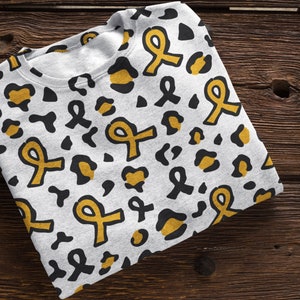 May include: A white sweatshirt with a black and gold leopard print pattern. The print features yellow ribbon designs.