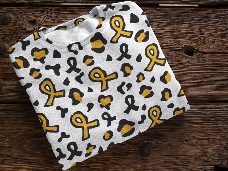 May include: A white sweatshirt with a black and gold leopard print pattern. The print features yellow ribbon designs.