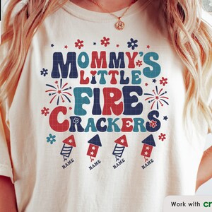 Puede incluir: Una camiseta blanca con un diseño rojo, blanco y azul que dice "Mommy's Little Firecrackers" con cuatro imágenes de fuegos artificiales debajo. El texto "Name" está debajo de cada imagen de fuegos artificiales.