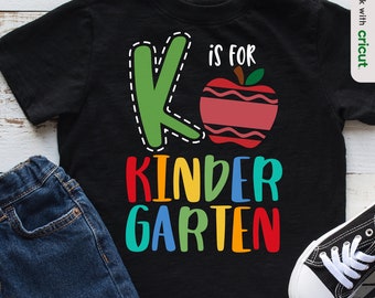 Könnte beinhalten: Ein schwarzes T-Shirt mit einem grünen Buchstaben K, einem roten Apfel mit einem weißen Biss und dem Text "K is for KINDERGARTEN" in Regenbogenfarben.