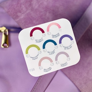 May include: A white square sticker sheet featuring seven circular labels with colored arches and leaf accents. The text reads: Actually Dramatic, Princess Behavior, Purse Full Of Polish, Unbothered Energy, Not Quiet Luxury, Neutral Territory, Lowkey Perfect, and F26.