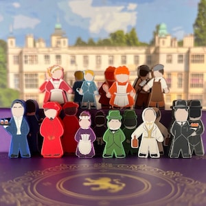May include: A set of 14 colorful wooden figurines depicting characters in various outfits and poses. The figurines are arranged in a row on a purple surface with a gold design.