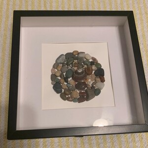 May include: A framed artwork featuring a circular arrangement of various colored and textured stones, creating a mosaic-like design.