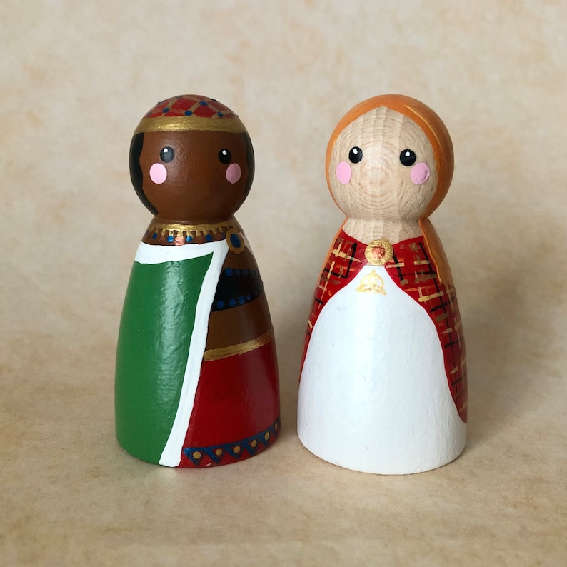 May include: Two wooden peg dolls dressed as kings. One doll has brown skin, a green and red robe, and a gold crown. The other doll has light skin, a red and white robe, and a gold crown.