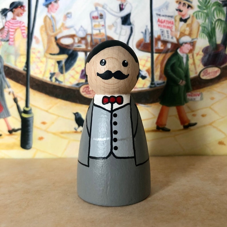 May include: A wooden peg doll painted to look like a man wearing a gray suit with a black vest and a red bow tie. The doll has a mustache and a friendly expression.