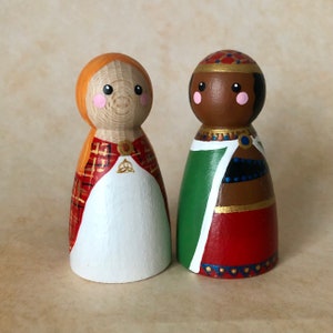 May include: Two wooden peg dolls, one with red and orange plaid and a white dress, the other with a green, red, and gold patterned robe.