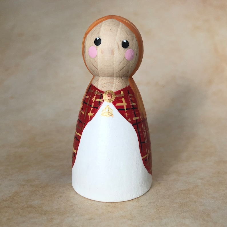 May include: A wooden peg doll with a red and gold plaid dress and a white face with pink cheeks.