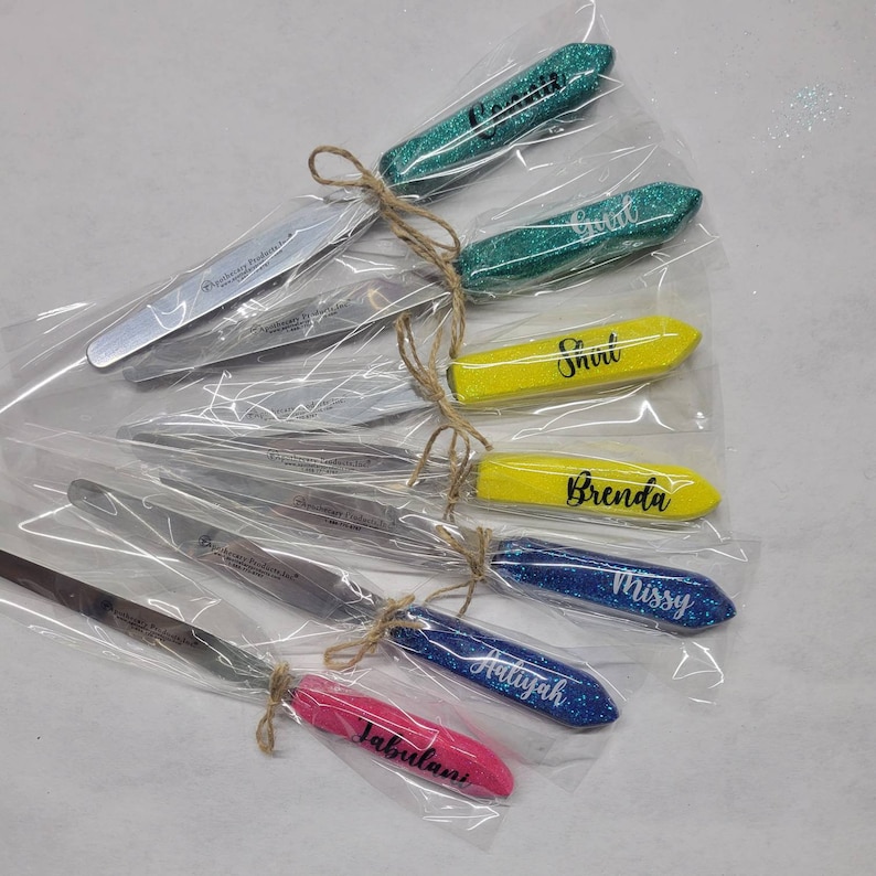 May include: A set of eight personalized spatulas with glitter handles. The spatulas are wrapped in clear plastic and tied with twine. The names on the spatulas are: "Corina", "Gail", "Shari", "Brenda", "Missy", "Atiyah", "Jabulani".