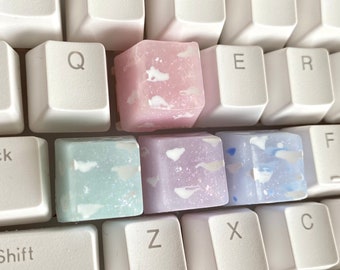 May include: Three different colored keycaps with a white speckled design. The keycaps are pink, purple, and blue.