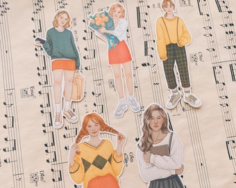 May include: Five illustrated stickers featuring women in various outfits. The stickers are printed on white paper with a light brown background. The stickers feature a woman with a bouquet of flowers, a woman in a plaid skirt, a woman in a sweater, a woman in a dress, and a woman in a sweater and skirt.