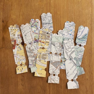 May include: A collection of vintage paper maps with street names and locations. The maps are in various shades of brown, yellow, and white, with black text. The maps are arranged in a fan shape, with the top of the maps pointing to the right.