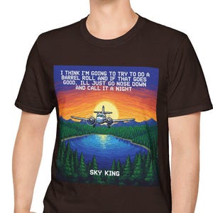 May include: A brown t-shirt featuring a pixelated graphic of a plane flying over a lake at sunset. The graphic includes the text "I THINK I'M GOING TO TRY TO DO A BARREL ROLL AND IF THAT GOES GOOD, ILL JUST GO NOSE DOWN AND CALL IT A NIGHT" and "SKY KING".