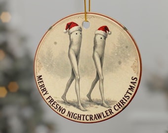 May include: Round Christmas ornament featuring two stylized figures with long legs, wearing Santa hats. The ornament has the text "MERRY FRESNO NIGHTCRAWLER CHRISTMAS" around the edge. The background is a vintage-style illustration.