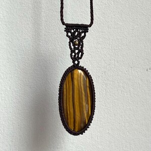 May include: A brown macrame necklace with a tiger's eye stone pendant.