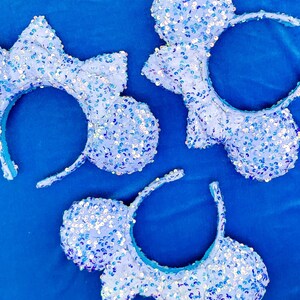 Peut inclure: Trois paires d'oreilles de Minnie Mouse en sequins bleus et blancs. Les oreilles sont faites d'un tissu doux et scintillant et sont parfaites pour ajouter une touche de magie Disney à n'importe quelle tenue.