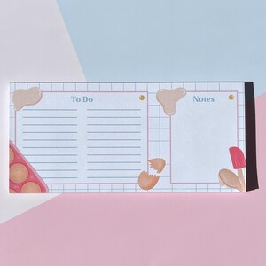 May include: A white notepad with a grid pattern and a blue and pink border. The notepad has two sections labelled "To Do" and "Notes". The "To Do" section has a broken egg and a muffin tin with brown batter. The "Notes" section has a red spatula and a brown spoon.