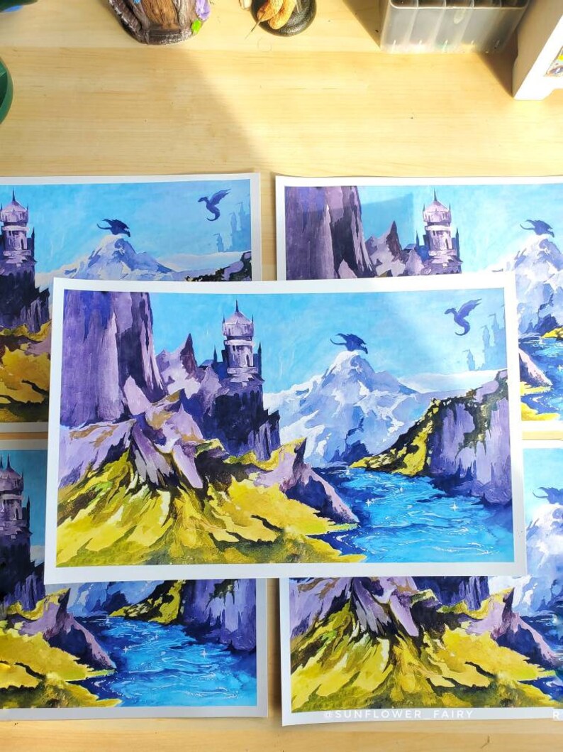 Puede incluir: Pinturas a la acuarela de un paisaje de fantas&iacute;a con monta&ntilde;as, un r&iacute;o y dragones voladores. La obra presenta un castillo, picos nevados y una vibrante paleta de colores azules, morados y amarillos. La firma del artista es visible.