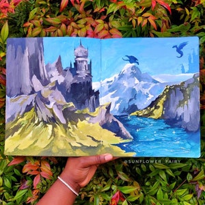 Puede incluir: Una pintura de paisaje de fantas&iacute;a con un castillo, monta&ntilde;as y dragones. La obra de arte est&aacute; en tonos de azul, gris, verde y amarillo. La pintura se sostiene contra un fondo de follaje verde y rojo.