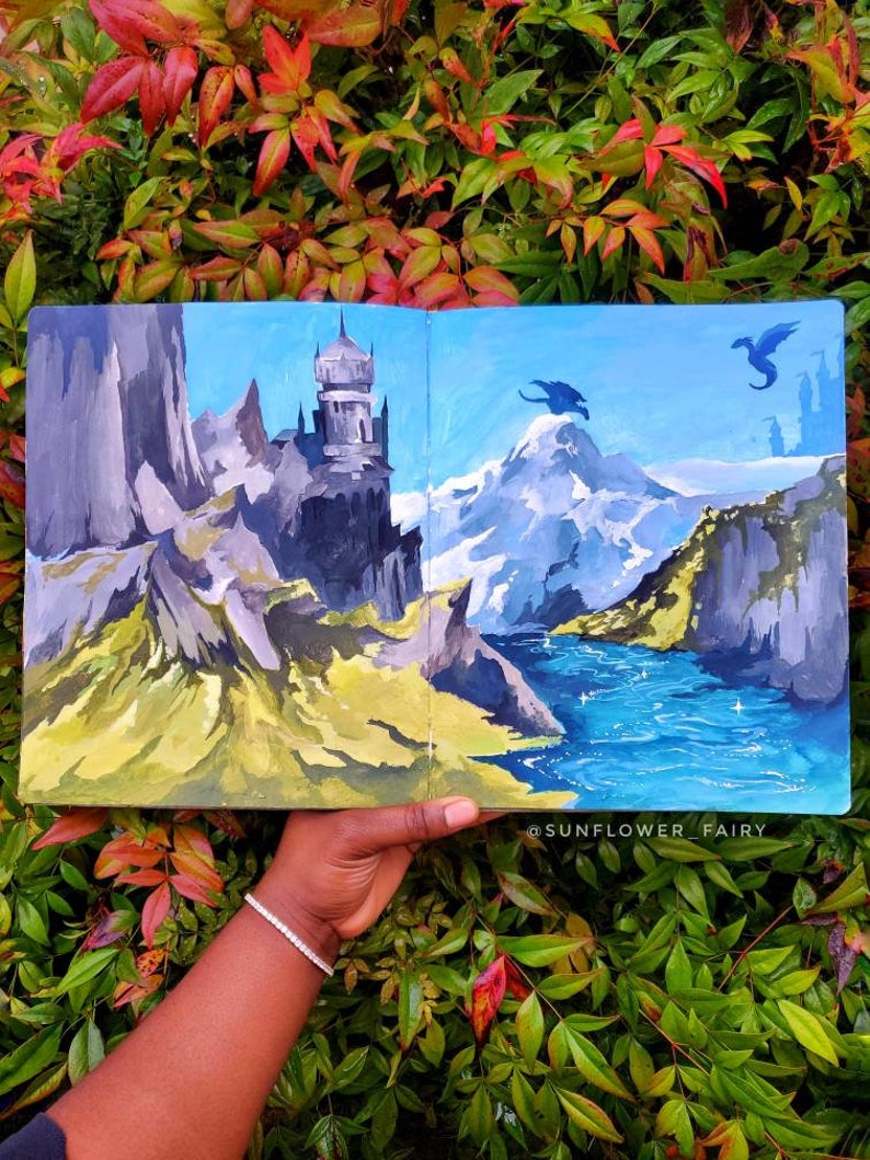 Puede incluir: Una pintura de paisaje de fantas&iacute;a con un castillo, monta&ntilde;as y dragones. La obra de arte est&aacute; en tonos de azul, gris, verde y amarillo. La pintura se sostiene contra un fondo de follaje verde y rojo.