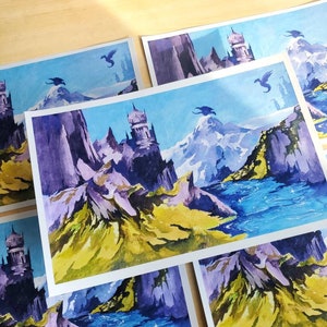 Puede incluir: Una colecci&oacute;n de pinturas de paisajes de fantas&iacute;a con dragones, castillos, monta&ntilde;as y agua. La obra de arte utiliza una paleta de azules, morados, verdes y amarillos. Las pinturas est&aacute;n sobre papel blanco y est&aacute;n dispuestas sobre una superficie de madera clara.
