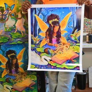 May include: A vibrant print of a fairy reading a book in a magical forest setting. The fairy has large orange wings and is surrounded by hummingbirds, a swan, and a frog. The artwork is rich in color, with blues, greens, and yellows dominating the scene.