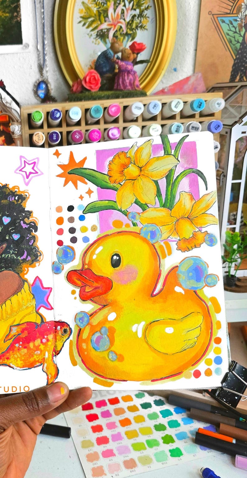 Puede incluir: Una ilustraci&oacute;n vibrante de un patito de goma amarillo con pico naranja y burbujas azules. Tambi&eacute;n se representan narcisos y un pez dorado. La obra de arte est&aacute; en una p&aacute;gina blanca, con una paleta de colores y marcadores en el fondo.