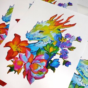 May include: Watercolor illustration of a dragon's head with vibrant colors. The dragon is surrounded by colorful flowers in shades of orange, pink, blue, and purple. The artwork is on white paper.