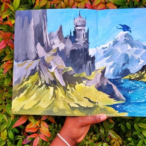 Puede incluir: Una pintura de paisaje que presenta un castillo en una monta&ntilde;a rocosa, un pico nevado y un drag&oacute;n azul. La obra de arte est&aacute; ambientada contra un cielo azul y una masa de agua. La pintura se sostiene contra un fondo de follaje verde y rojo.