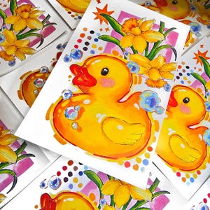 Puede incluir: Impresiones art&iacute;sticas en acuarela que presentan un alegre patito de goma amarillo con pico rojo y mejillas rosas, rodeado de burbujas y narcisos amarillos. La obra de arte tiene un estilo caprichoso con acentos coloridos y un tema l&uacute;dico.