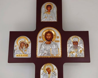 May include: A wooden cross with five silver and gold icons depicting religious figures. The icons are framed in gold and silver and are set against a dark brown background.