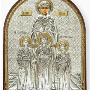 May include: A religious icon featuring a central figure with a halo, holding a cross, and three smaller figures below. The artwork is primarily silver and gold, set within a dark brown wooden frame. The background has a textured, mosaic-like appearance.