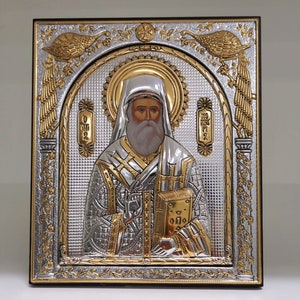 May include: Silver and gold icon of a religious figure with a beard and a book in their hand. The icon is framed in a wooden frame with a gold and silver design.
