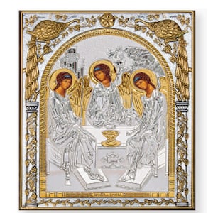 May include: A silver and gold icon depicting the Holy Trinity. Three figures with wings are seated around a chalice. The icon is framed with a gold border and intricate floral designs.