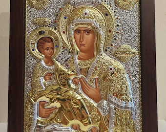 May include: A gold and silver icon depicting the Virgin Mary holding the baby Jesus. The icon is framed in a dark wood frame.