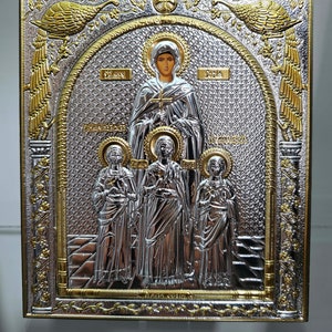 May include: Silver and gold icon depicting the Virgin Mary and three saints. The icon is framed in a gold and silver frame with a floral design. The icon is set against a white background.