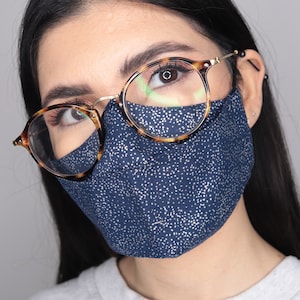 May include: A woman wearing a navy blue face mask with white polka dots and tortoise shell glasses. The mask covers her nose and mouth.