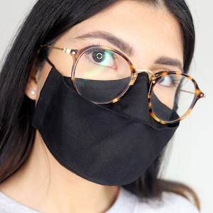 May include: A person wearing a black face mask and tortoise shell glasses. The person is wearing a light gray sweatshirt.