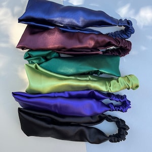 May include: Six satin headbands in various colors, including navy blue, burgundy, green, light green, purple, and black. Each headband has a gathered elastic band at the back.