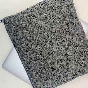 May include: A gray laptop sleeve with a black leopard print pattern. The sleeve is quilted and has a zipper closure.