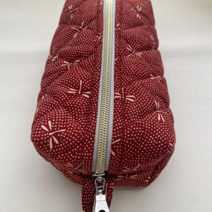 May include: A red quilted zippered pouch with a white dragonfly pattern. The pouch has a silver zipper pull.