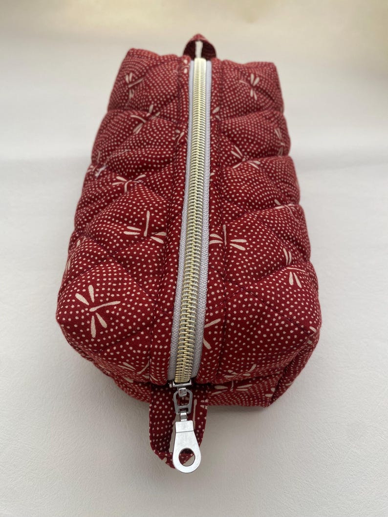 May include: A red quilted zippered pouch with a white dragonfly pattern. The pouch has a silver zipper pull.