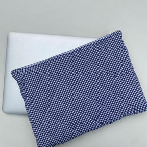 May include: A blue and white gingham pattern quilted laptop sleeve with a silver zipper. The sleeve is rectangular and appears to be made of fabric. The sleeve is resting on top of a white laptop.